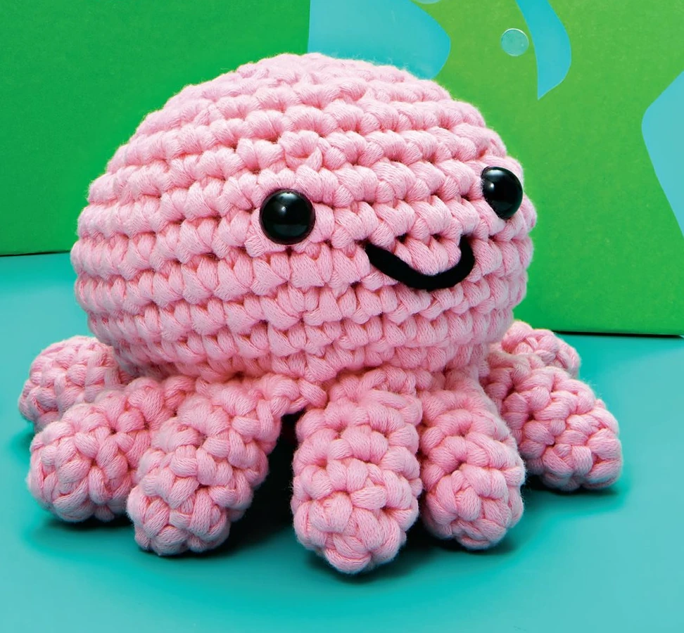 Full finished pink crochet octopus pictured on turquoise set, from the authorized original pattern photo